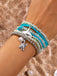 Accumulation de bracelets de perles avec un pendentif tortue au poignet sur fond sableux