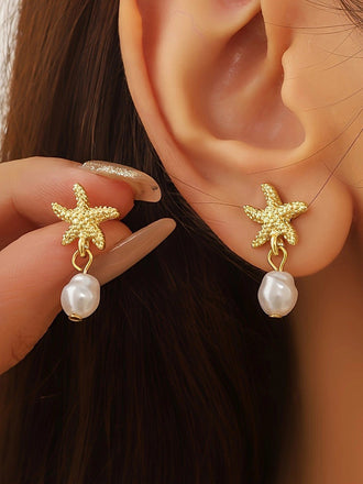 Boucles d'oreilles en forme d'étoile de mer dorée avec des gouttes de perles, portées par une personne.