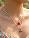 Pearl necklace with cherry pendants worn by a person outdoors