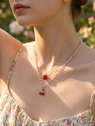 Femme portant une robe à fleurs et un délicat collier à pendentifs cerises sur fond naturel flou