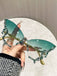 Sunglasses with decorative gold and green frame held by a hand against a neutral background