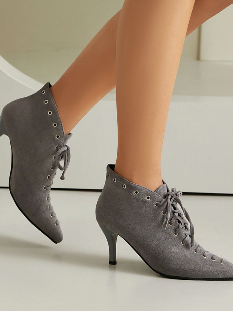 Gray high-heeled shoes with lace-up design worn by a person on a neutral background