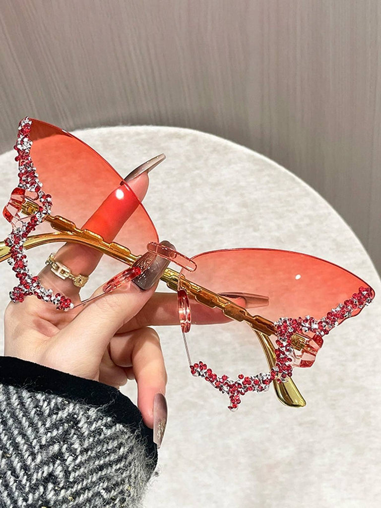 Sunglasses with red lenses and gold frame held by a hand against a neutral background