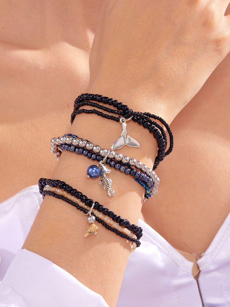 Multiple bracelets with charms on a wrist against a light background