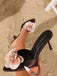 A hand holding one dark brown satin mule to show the detail of the bi-color 3D flower.