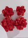 A pair of red statement earrings with multiple tiered fabric flower petals arranged in a cluster on a plain background.