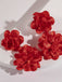 Detail shot of red oversized fabric flower earrings showing the layered texture and 3D floral cluster design.