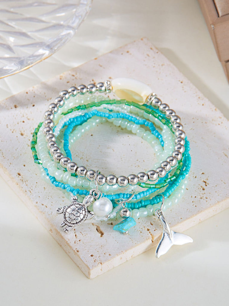 Stack of beaded bracelets with charms on a textured stone surface