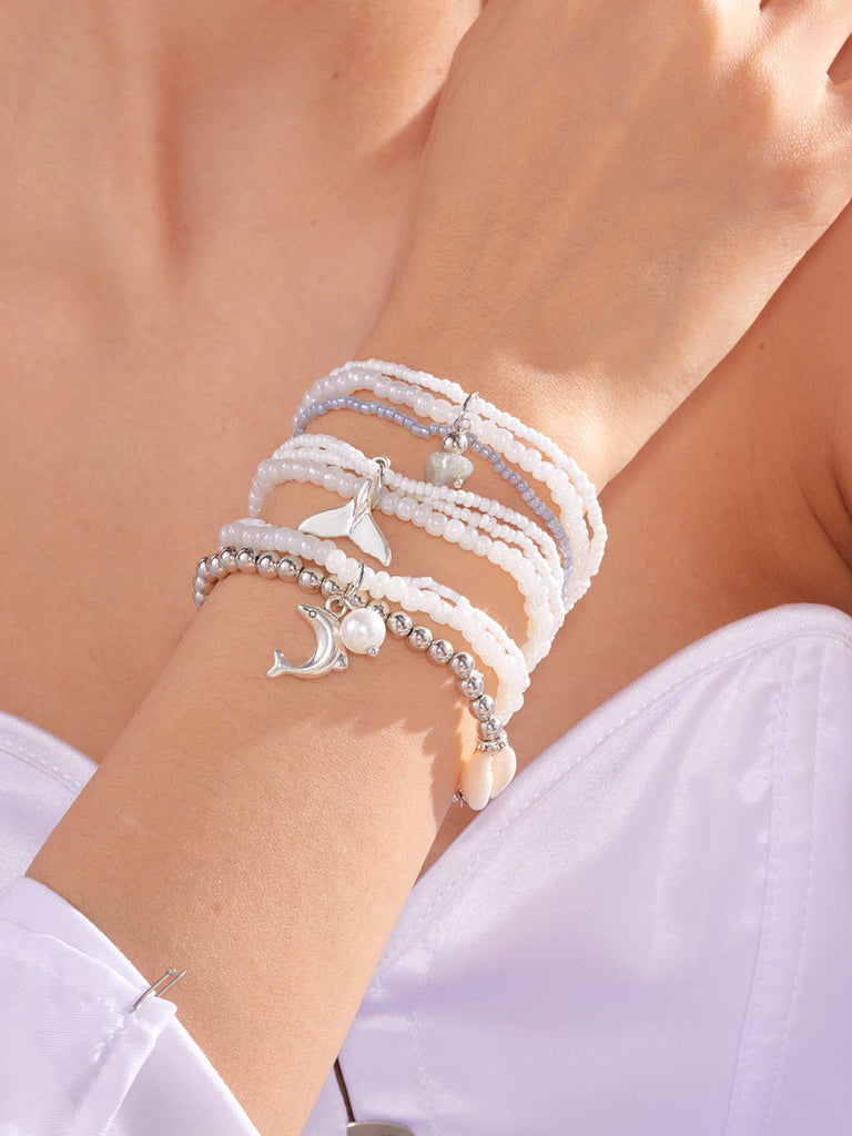 Close-up of a wrist wearing multiple white beaded bracelets with silver anchor charms.